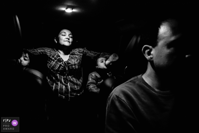 A mother sits in the back seat of a car with her two young children as their father drives in this family picture by a Florianopolis photographer. 