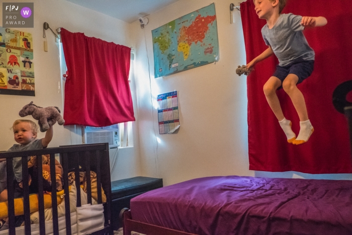 A boy jumps on his bed as his baby brother plays in his crib in this photograph by a Los Angeles, CA documentary family photographer. 