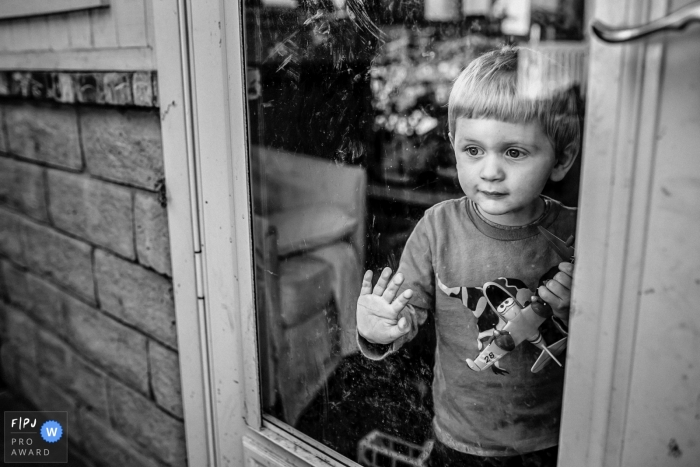 Photo by: <a href="https://www.fpja.com/documentary-family-photography-contests/annie-bang/los-angeles/2085466">Annie Bang - United States</a> A young boy looks out the window as he holds a toy plane in this image created by a Los Angeles, CA family photographer.