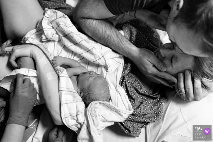 Photo by: <a href="https://www.fpja.com/documentary-family-photography-contests/benjamin-lipford/atlanta/2085616">Benjamin Lipford - United States</a> A husband hugs his wife as she holds her baby in the hospital in this birth picture by an Atlanta, GA photographer.