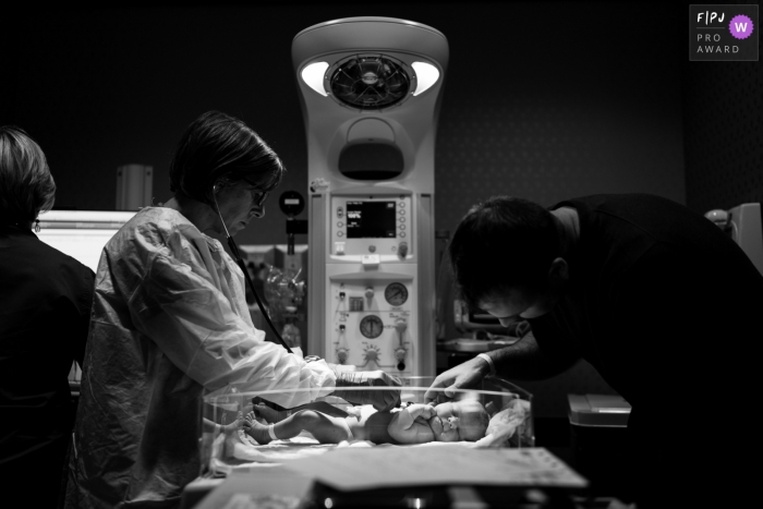 Photo by: <a href="https://www.fpja.com/documentary-family-photography-contests/benjamin-lipford/atlanta/2085621">Benjamin Lipford - United States</a> A nurse checks a newborn's heartbeat in the hospital as the father visits in this black and white photo created by an Atlanta, GA birth photographer.