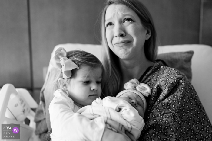 Photo by: <a href="https://www.fpja.com/documentary-family-photography-contests/benjamin-lipford/atlanta/2085631">Benjamin Lipford - United States</a> A mother tears up as she and her young daughter hold her newborn infant in the hospital bed in this black and white photo composed by an Atlanta, Georgia documentary birth photographer.