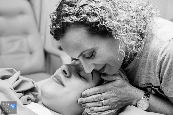 Photo by: <a href="https://www.fpja.com/documentary-family-photography-contests/gisele-soares/rio-de-janeiro/2085671">Gisele Soares - Brazil</a> A woman embraces a mother who has just given birth in the hospital in this black and white picture captured by an award-winning Rio de Janeiro, Brazil birth photographer.