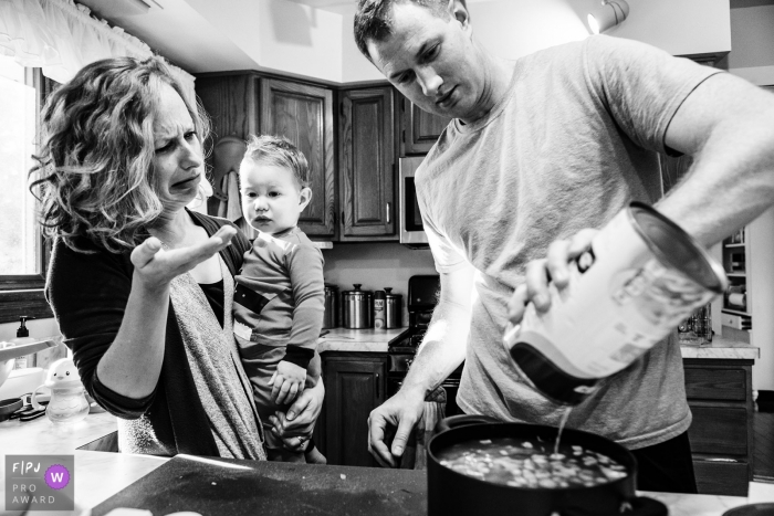 Photo by: <a href="https://www.fpja.com/documentary-family-photography-contests/colie-james/boulder/2085716">Colie James - United States</a> A mother and child look uncertain as a father pours canned soup into a pot on the stove in this FPJA award-winning picture by a Boulder, CO family photographer.