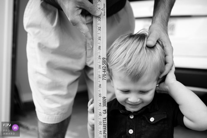 Photo by: <a href="https://www.fpja.com/documentary-family-photography-contests/benjamin-lipford/atlanta/2085721">Benjamin Lipford - United States</a> Atlanta, Georgia family session photo of a toddler getting height measured with a yardstick by dad.