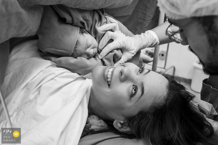 Rio Grande do Sul birth photojournalist captured this black and white portrait of a new mom smiling up at her partner while their newborn baby is laid on her chest