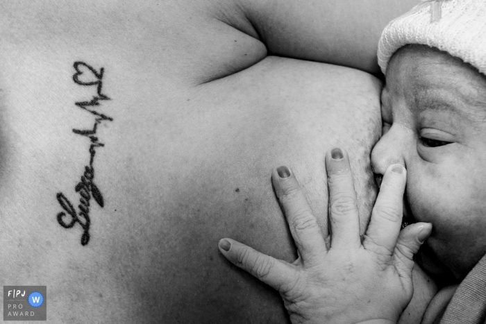 Photo en gros plan en noir et blanc d'un nouveau-né tenant l'épaule tatouée de sa mère, prise par un photographe documentaire de naissance du Rio Grande do Sul, au Brésil.