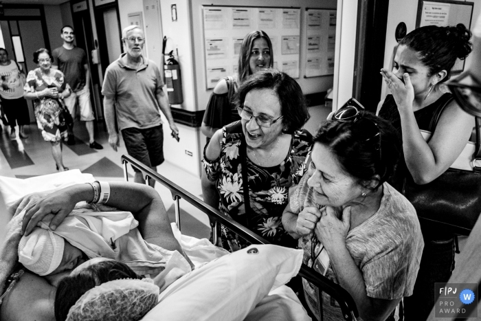 Photo by: <a href="https://www.fpja.com/documentary-family-photography-contests/rafael-rosa/rio-grande-do-sul/2085871">Rafael Rosa - Brazil</a> A woman's family surrounds her in the hospital to meet her newborn baby in this black and white photo captured by a Rio Grande do Sul, Brazil birth photographer.