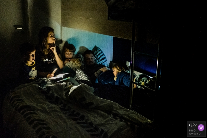 Photo by: <a href="https://www.fpja.com/documentary-family-photography-contests/rafael-rosa/rio-grande-do-sul/2085901">Rafael Rosa - Brazil</a> A mother uses her phone light to read a bedtime story to her sons while her husband sleeps in this FPJA award-winning image captured by a Rio Grande do Sul, Brazil family photographer.