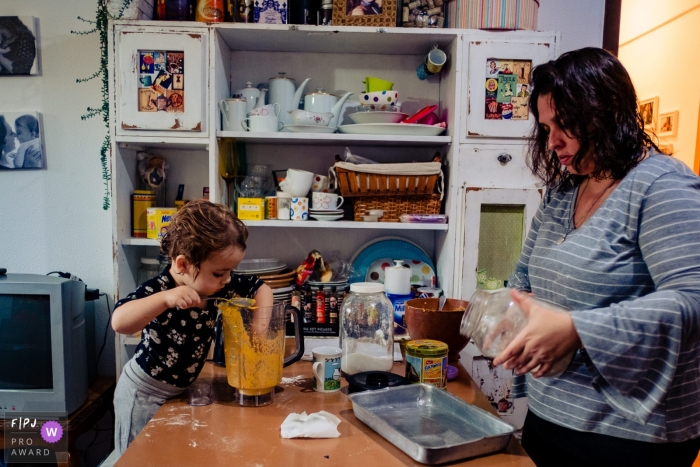 A little girl reaches her hand into a mixture while her mother reads a jar label in this award-winning photo by a Rio Grande do Sul, Brazil family photographer.