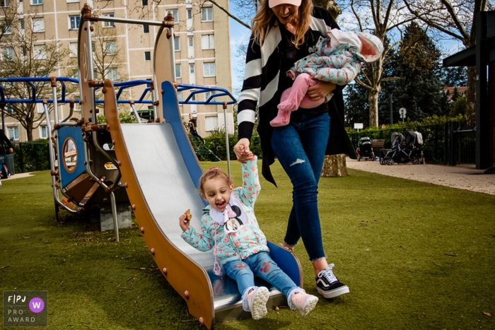 Photo by: <a href="https://www.fpja.com/documentary-family-photography-contests/rafael-rosa/rio-grande-do-sul/2085966">Rafael Rosa - Brazil</a> A mother helps her daughter down a slide with one hand as she carries her baby in another in this photo by a Rio Grande do Sul, Brazil award-winning family photographer.