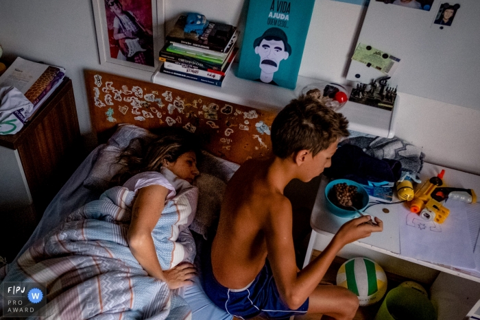 Photo by: <a href="https://www.fpja.com/documentary-family-photography-contests/rafael-rosa/rio-grande-do-sul/2085976">Rafael Rosa - Brazil</a> A boy eats cereal as his mom lays in his bed in this photograph created by a Rio Grande do Sul, Brazil family photojournalist.