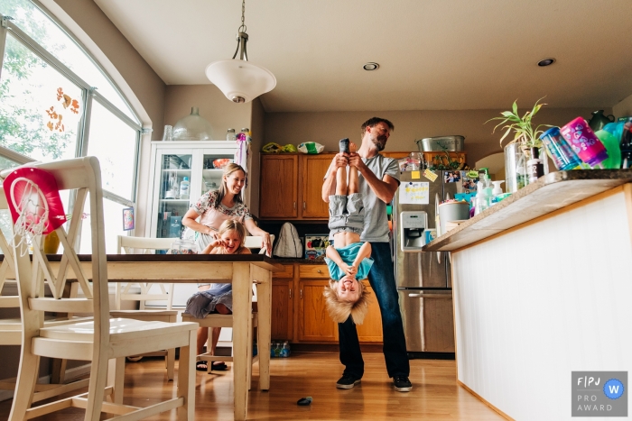 A father holds his son upside down as his mom and sister laugh in this documentary-style family image recorded by a Boulder, CO photographer. 