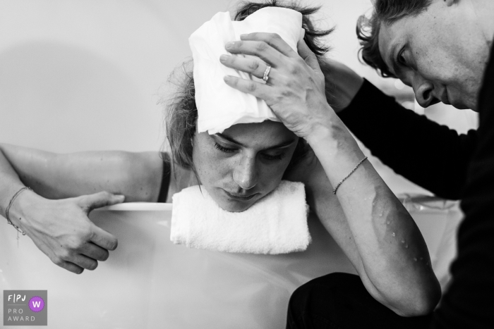 A husband supports his wife as she leans over the edge of the birthing tub during her at-home birth in this black and white photo by a Copenhagen birth photographer.