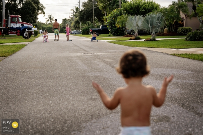 A family rides bikes and scooters down a street while a diaper clad toddler follows behind in this photo captured by a Key West vacation photographer