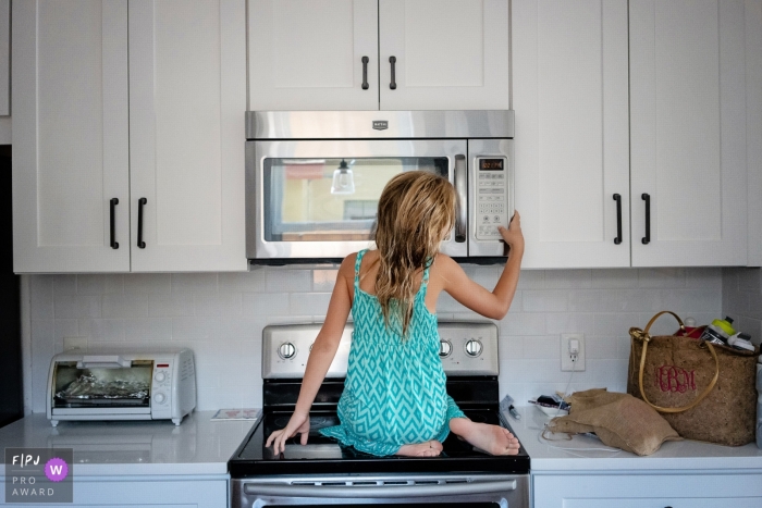 Une jeune fille est assise sur le poêle pour atteindre le micro-ondes dans le cadre de ce concours récompensant une photo de la famille Photojournalist Association, créé par un photographe de famille de Key West, en Floride.