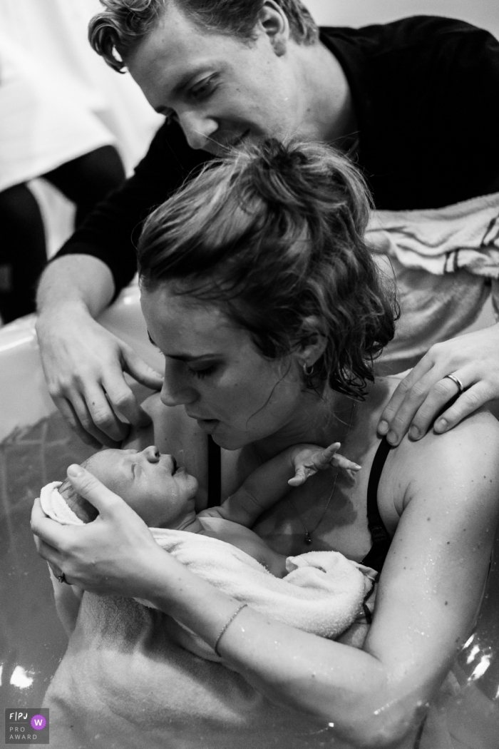 Photo: <a href="https://www.fpja.com/documentary-family-photography-contests/jess-lycoops/copenhagen/2086106"> Jess Lycoops - Danemark </a> Un père observe la femme qui tient son nouveau-né dans la baignoire d'accouchement. Cette image en noir et blanc a été capturée par un photographe de naissance primé de Copenhague.