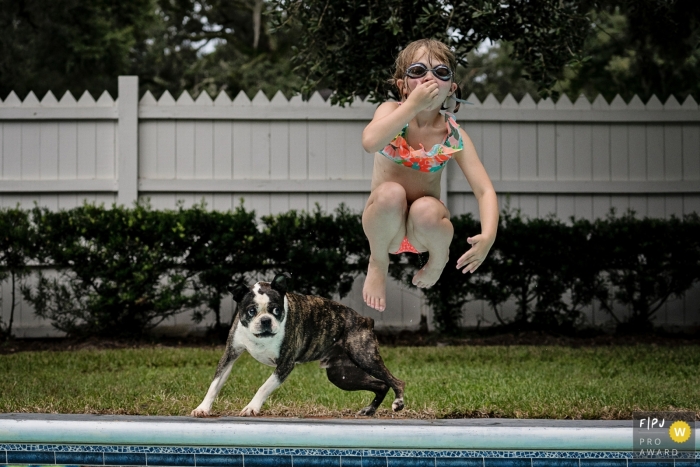 Photo by: <a href="https://www.fpja.com/documentary-family-photography-contests/julie-ambos/key-west/2086171">Julie Ambos - United States</a> Key West family photojournalist captured this image of a child jumping into a pool while her dog follows suit