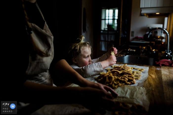 Photo by: <a href="https://www.fpja.com/documentary-family-photography-contests/jess-lycoops/copenhagen/2086206">Jess Lycoops - Denmark</a> A little girl picks up a cookie from a pile her mother has just baked in this family picture by a Copenhagen photographer.