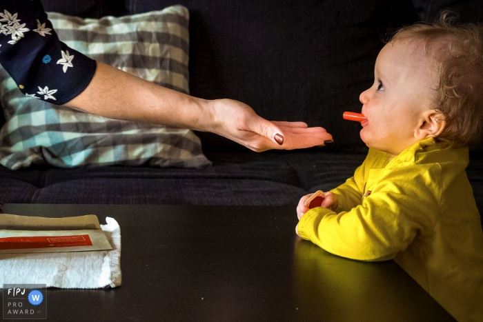 Photo by: <a href="https://www.fpja.com/documentary-family-photography-contests/katrin-k%C3%BCllenberg/dusseldorf/2086416">Katrin Küllenberg - Germany</a> A woman's hand is held out expectantly for the marker cap in her toddlers mouth in this photo captured by a North Rhine-Westphalia documentary family photographer