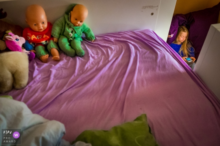 North Rhine-Westphalia documentary family photographer captured this photo of a young girl watching her phone as an empty bed full of baby dolls stands in the foreground