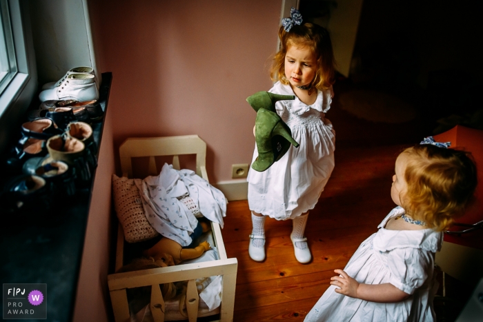 Le photographe de famille documentaire Wallonie a capturé cette photo de deux filles en robes blanches inspectant une paire de talons hauts verts