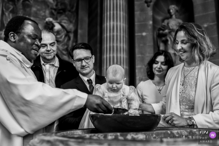 Photo by: <a href="https://www.fpja.com/documentary-family-photography-contests/maryline-krynicki/%C3%AEle-de-france/2088011">Maryline Krynicki - France</a> France documentary family photographer captured this black and white photo of a baby's baptism with a priest inside a church.