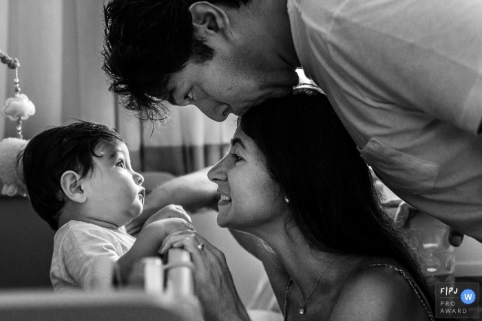 This black and white photo of a young baby looking at his father kiss the top of his mothers head was captured by a Sao Paulo documentary style family photographer