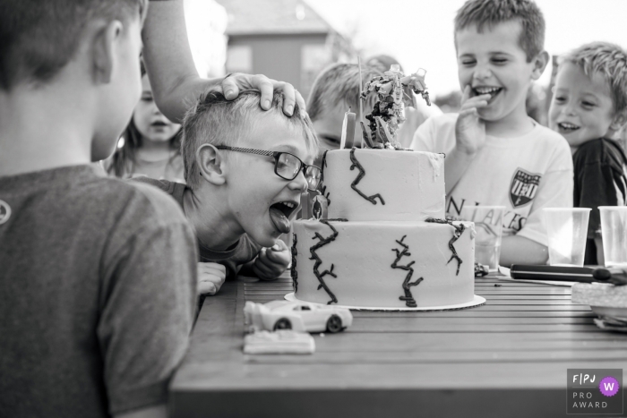 Kansas City documentary style family photographer captured this photo of a young boy licking his birthday cake surrounded by his laughing friends