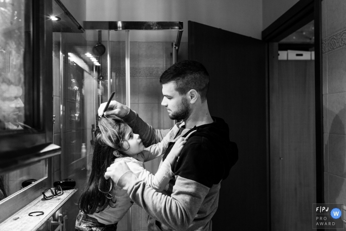 A father combs his daughter's hair in the bathroom in this family picture by a Modena photographer. 