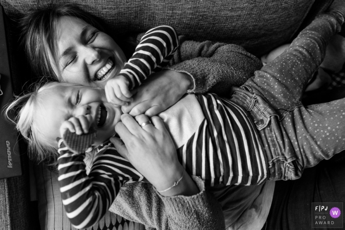 Une mère tient sa fille dans ses bras alors qu’elle est allongée sur le canapé et rit dans cette photo prise par un photographe de la famille du documentaire de Modène.