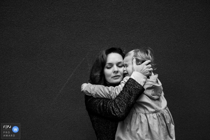 A mother holds her crying baby girl in this photo recorded by an Antwerpen award-winning, documentary-style family photographer. 