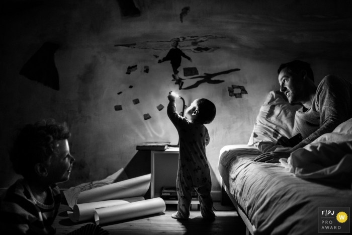 A little boy plays with a lamp while his father and brother watch in this photo by an Antwerpen award-winning family photographer. 