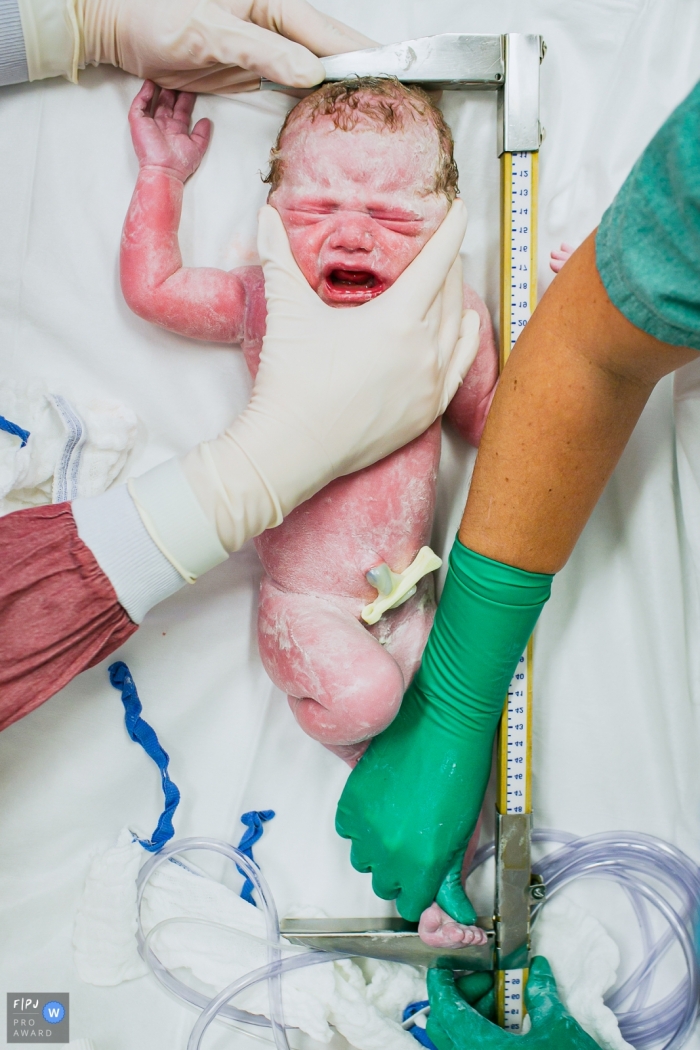 Two nurses measure a newborn baby in the hospital in this photo captured by an award-winning Sao Paulo, Brazil birth photographer.