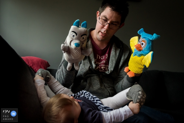 Photo by: <a href="https://www.fpja.com/documentary-family-photography-contests/yvette-vlaar/amsterdam/2090231">Yvette Vlaar - Netherlands</a> A father plays with two puppets while his baby boy watches in this photo recorded by an Amsterdam award-winning, documentary-style family photographer.