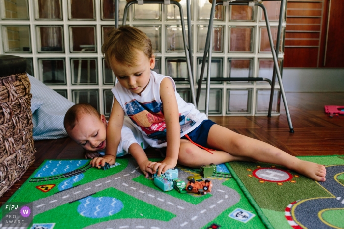 Two brothers play with toy cars on the floor in this photo recorded by an Aveiro, Portugal award-winning, documentary-style family photographer. 