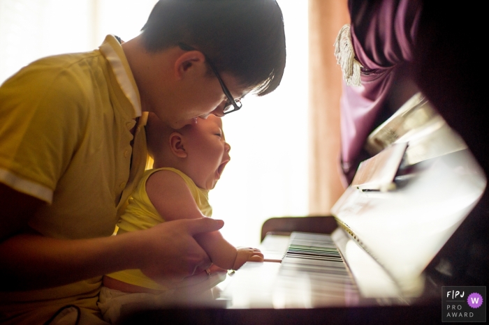 A father helps his baby play the piano in this photograph created by a Hangzhou City family photojournalist. 