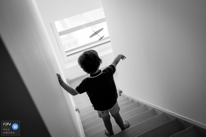 Photo by: <a href="https://www.fpja.com/documentary-family-photography-contests/sybil-rondeau/nantes/2090856">Sybil Rondeau - France</a> A little boy flies a toy airplane down the stairs in this documentary-style family image recorded by a Nantes photographer.