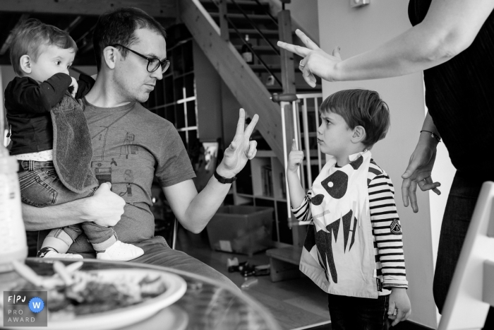 Photo by: <a href="https://www.fpja.com/documentary-family-photography-contests/sybil-rondeau/nantes/2090926">Sybil Rondeau - France</a> A father and mother hold up two fingers while their son argumentatively holds up one in this photograph by a Nantes documentary family photographer.