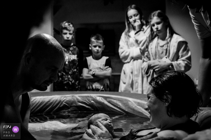 Photo by: <a href="https://www.fpja.com/documentary-family-photography-contests/annemiek-kinneging/drenthe/2091366">Annemiek Kinneging - Netherlands</a> Children surround their mother in her birthing tub to meet their newborn sibling in this black and white photo by a Drenthe, Netherlands birth photographer.