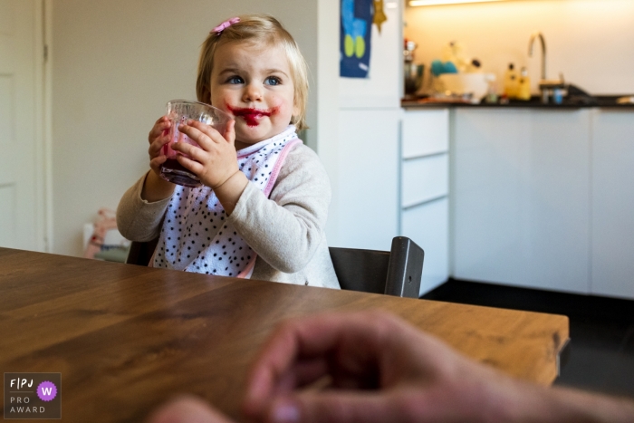 Photo by: <a href="https://www.fpja.com/documentary-family-photography-contests/gonda-meurs/noord-holland/2091571">Gonda Meurs - Netherlands</a> A little girl looks up with grape juice on her face after taking a sip from her cup in this image created by a Netherlands family photographer.