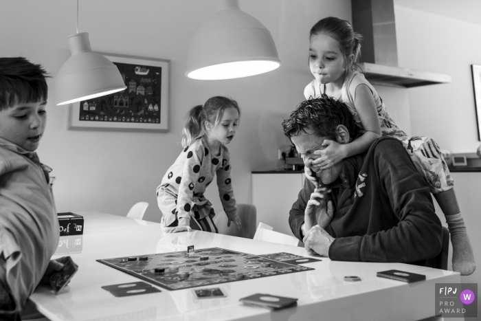 Une famille joue à un jeu de société alors qu'une petite fille grimpe sur les épaules de son père sur cette photo prise par un photographe de famille de style documentaire primé aux Pays-Bas.