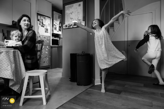 Photo by: <a href="https://www.fpja.com/documentary-family-photography-contests/annie-gozard/paris/2092261">Annie Gozard - France</a> Two little girls dance around while their mother watches in this documentary-style family image recorded by a Paris, France photographer.
