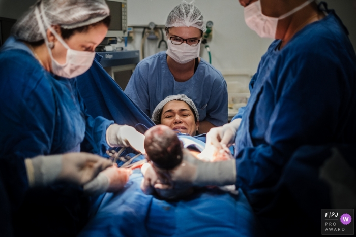 Photo by: <a href="https://www.fpja.com/documentary-family-photography-contests/emanuelle-rigoni/recife/2092386">Emanuelle Rigoni - Brazil</a> Nurses show a mother her newborn for the first time after her hospital birth in this image captured by a Recife birth photographer.