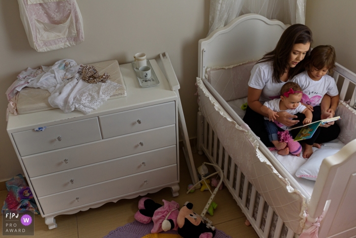 Photo by: <a href="https://www.fpja.com/documentary-family-photography-contests/emanuelle-rigoni/recife/2092396">Emanuelle Rigoni - Brazil</a> A mother sits in a crib with her children reading a book in this FPJA award-winning picture by a Recife family photographer.