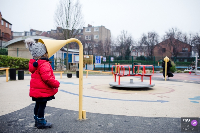 Photo by: <a href="https://www.fpja.com/documentary-family-photography-contests/ana-ruivo/london/2092656">Ana Ruivo - United Kingdom</a> A little girl speaks into a playground talk tube while her mother listens on the other side in this FPJA award-winning image captured by a London, England family photographer.