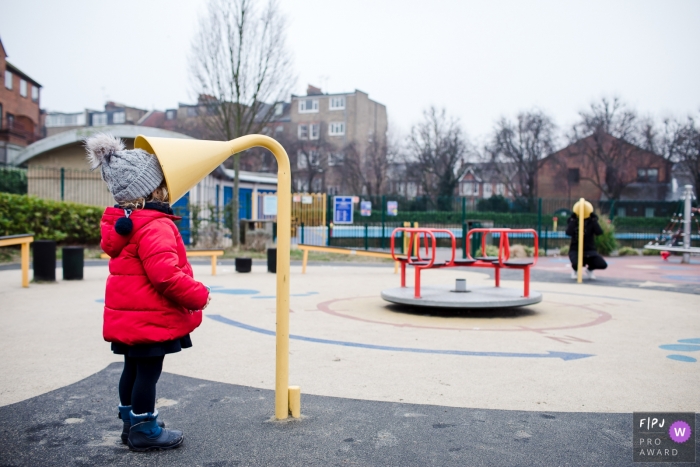 Une petite fille parle dans un tube de conversation en terrain de jeu pendant que sa mère écoute de l'autre côté dans cette image primée du FPJA, capturée par un photographe de famille à Londres, en Angleterre.