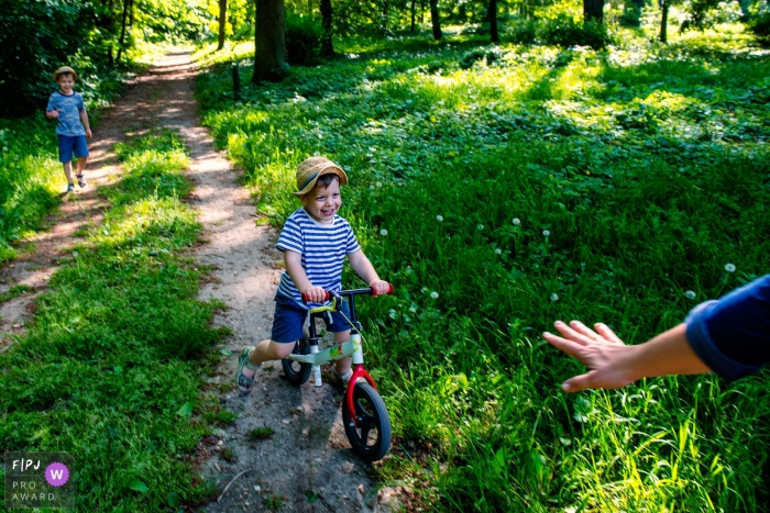 Un petit garçon sourit en faisant du vélo sur un sentier pendant que son frère marche derrière sur cette photo primée d'un photographe de famille de Budapest, en Hongrie.