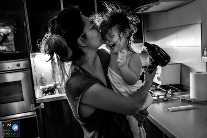 A little girl laughs as her mother blow dries her hair in this award-winning photo by an Essex, England family photographer.