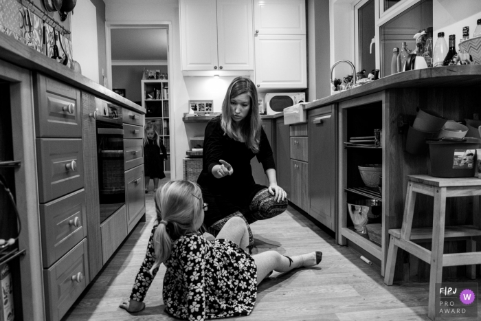 Photo by: <a href="https://www.fpja.com/documentary-family-photography-contests/raluca-chase/essex/2093336">Raluca Chase - United Kingdom</a> A mother scolds her daughter who sits on the kitchen floor in a nice dress in this image created by an Essex, England family photographer.